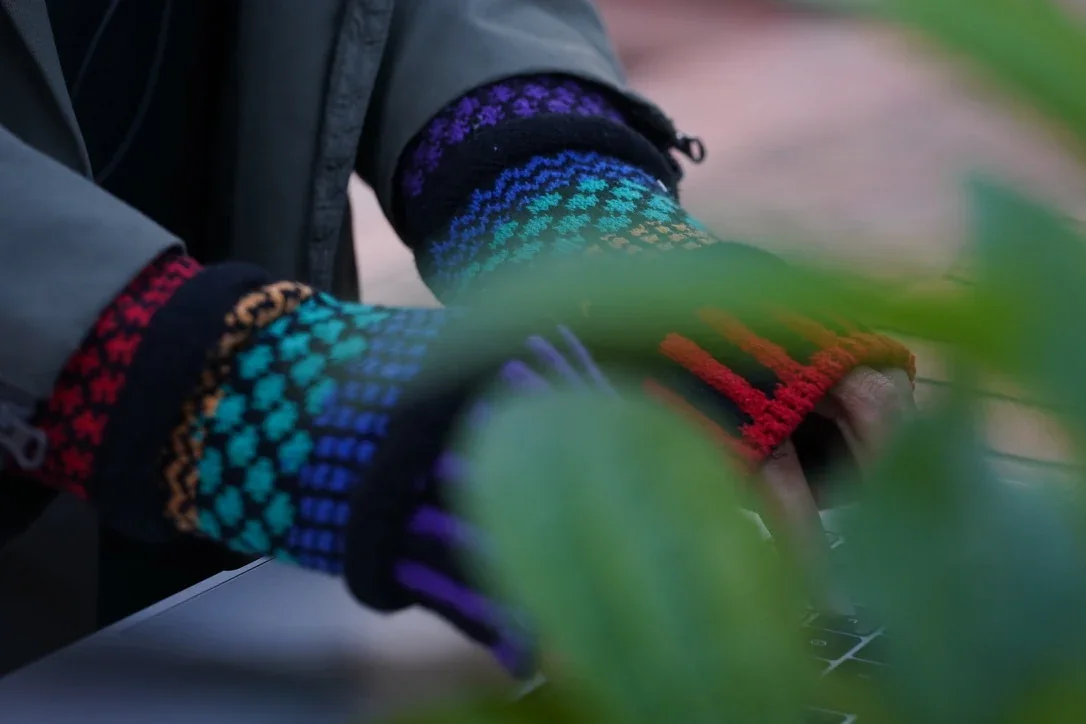 Color and knit texture — fingerless gloves framed by greenery.