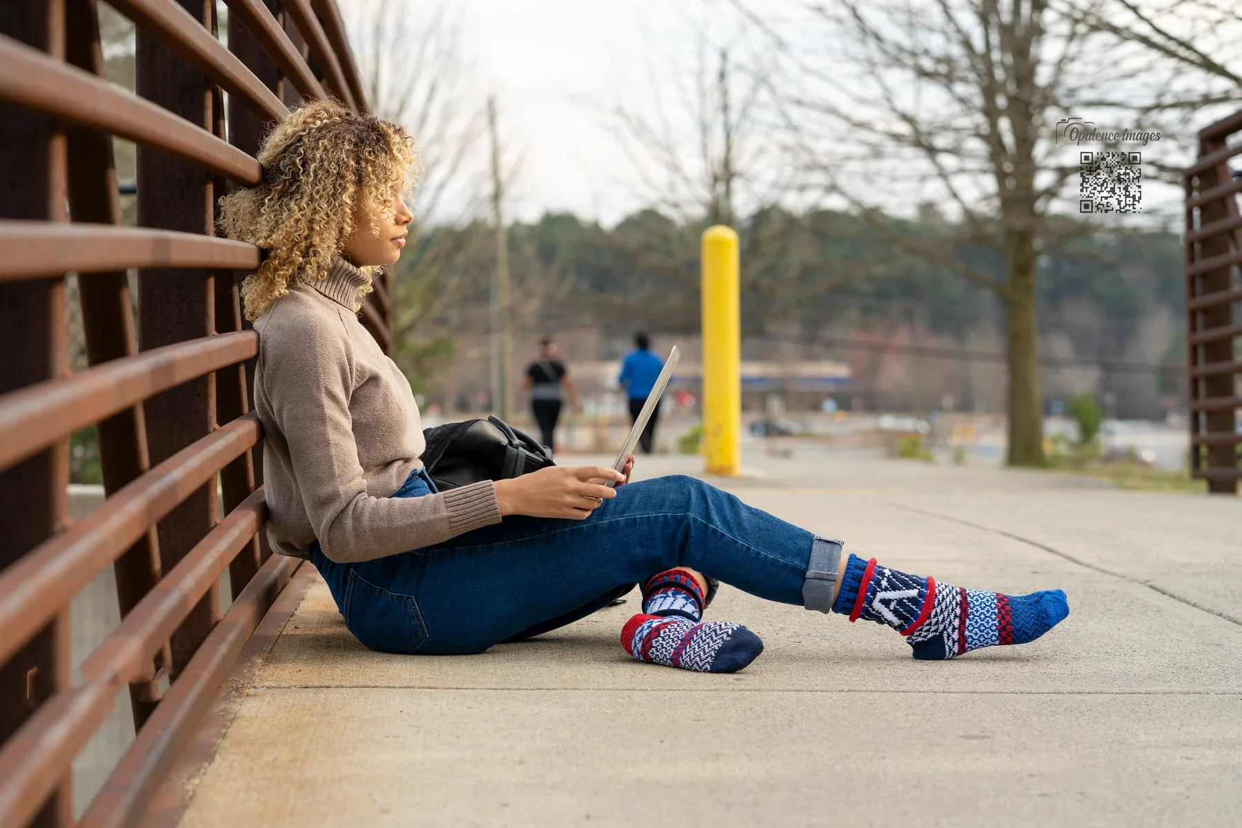 Relaxing with a tablet beside a bridge railing, wearing colorful patterned socks.