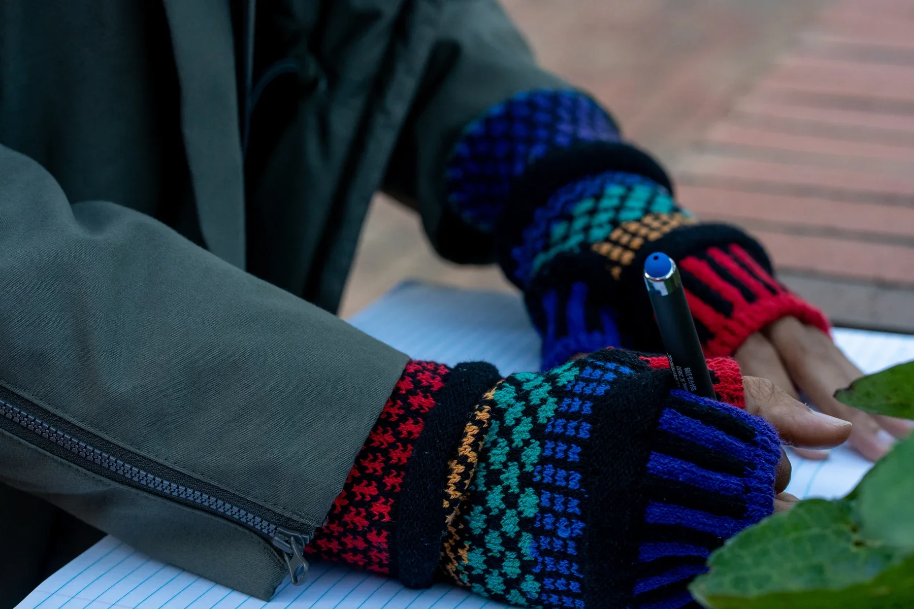 Close view of patterned fingerless gloves, a pen, and an open notebook.